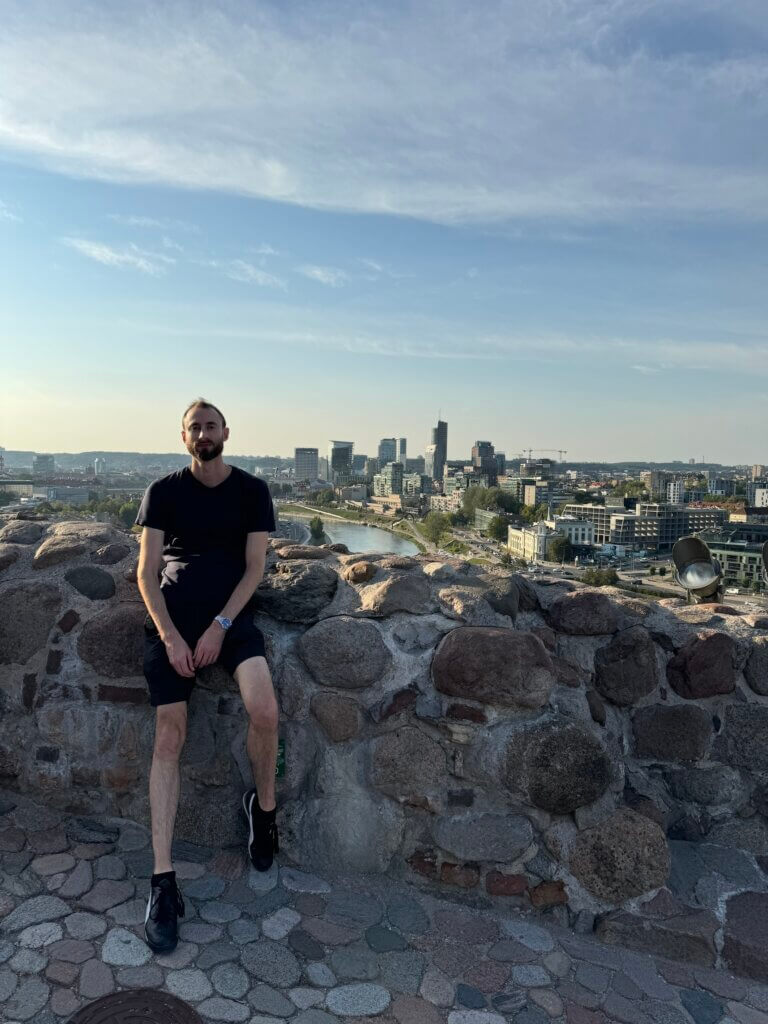 Edward Sturm in Vilnius, Lithuania in 2024. The city of Vilnius looms in the background, behind Edward, who looks casual and cool in the Baltic afternoon.