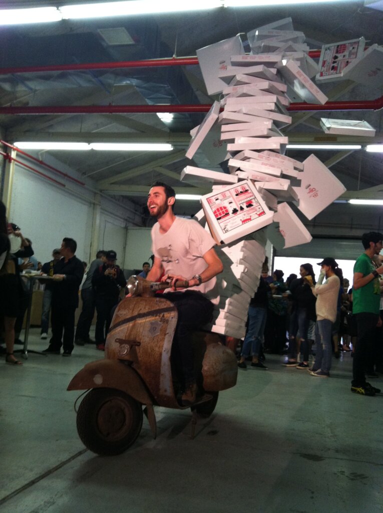 Edward Sturm on a motorcycle with pizza boxes falling behind him. Exhibit at the World's Largest Pizza Party - thrown by A Razor, A Shiny Knife - in Williamsburg, NYC 2014.