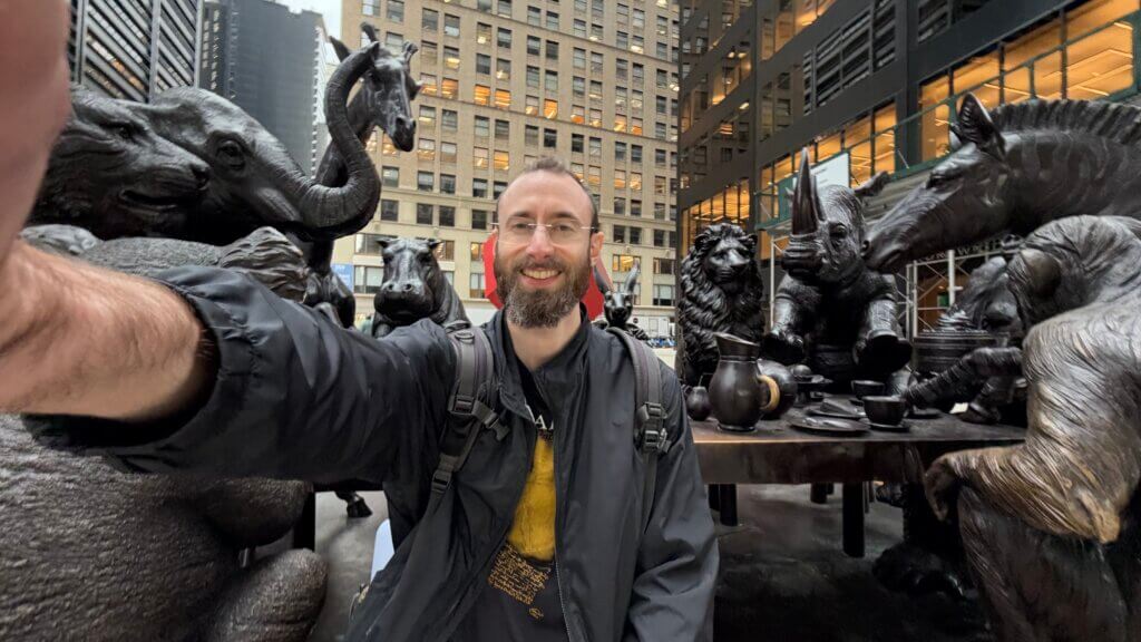 Edward Sturm sitting at the bronze Wild Table of Love statue by Gillie and Marc in Lower Manhattan, 2026.