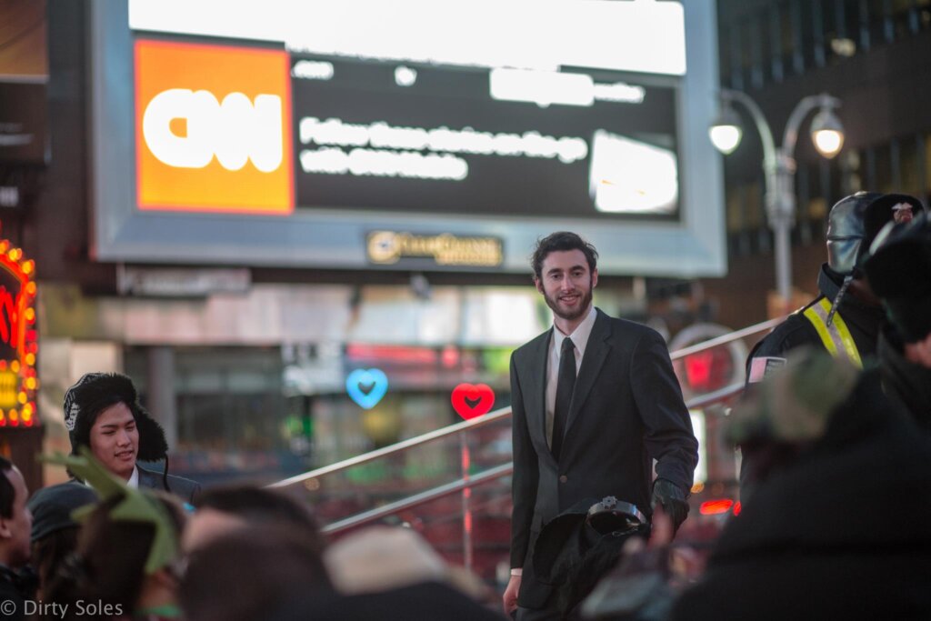 Edward Sturm in a suit, standing atop the TDF’s TKTS Steps, being photographed during the filming of "Harlem Shake NYC" in 2013.