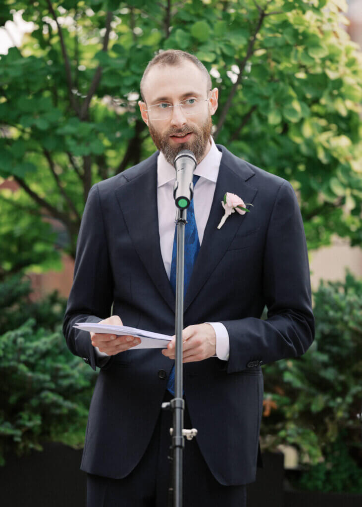 Close-up of Edward Sturm in a beautiful suit with a boutonniere on his lapel, officiating his brother's wedding in Chicago in 2026.