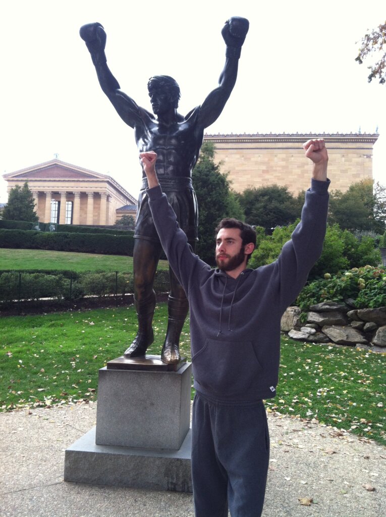 Edward Sturm in a sweatsuit, posing with the Rocky Statue at the Philadelphia Museum of Art in 2013.