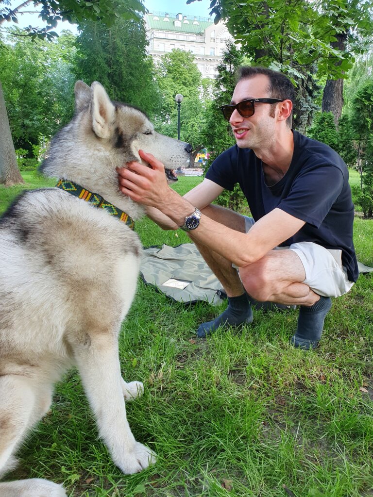 Edward Sturm smiling, crouching with a husky dog. Photo taken in Taras Shevchenko Park in Kyiv, Ukraine in 2020.