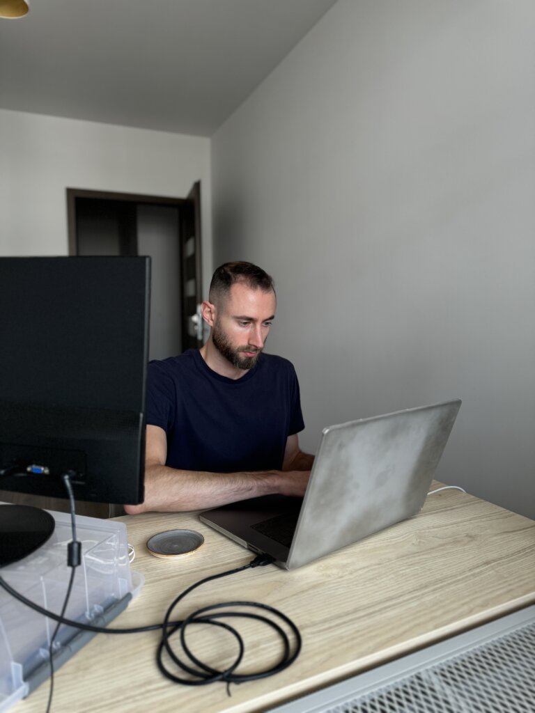 Edward Sturm in a dark blue shirt behind a laptop and external monitor. Photo taken in 2024.