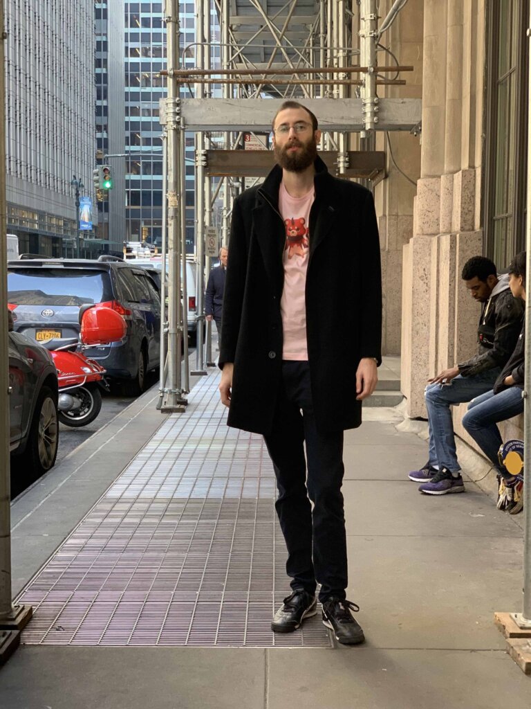 Edward Sturm in a Matchstick World of Ether shirt and black coat on the streets of Midtown, NYC in 2018.