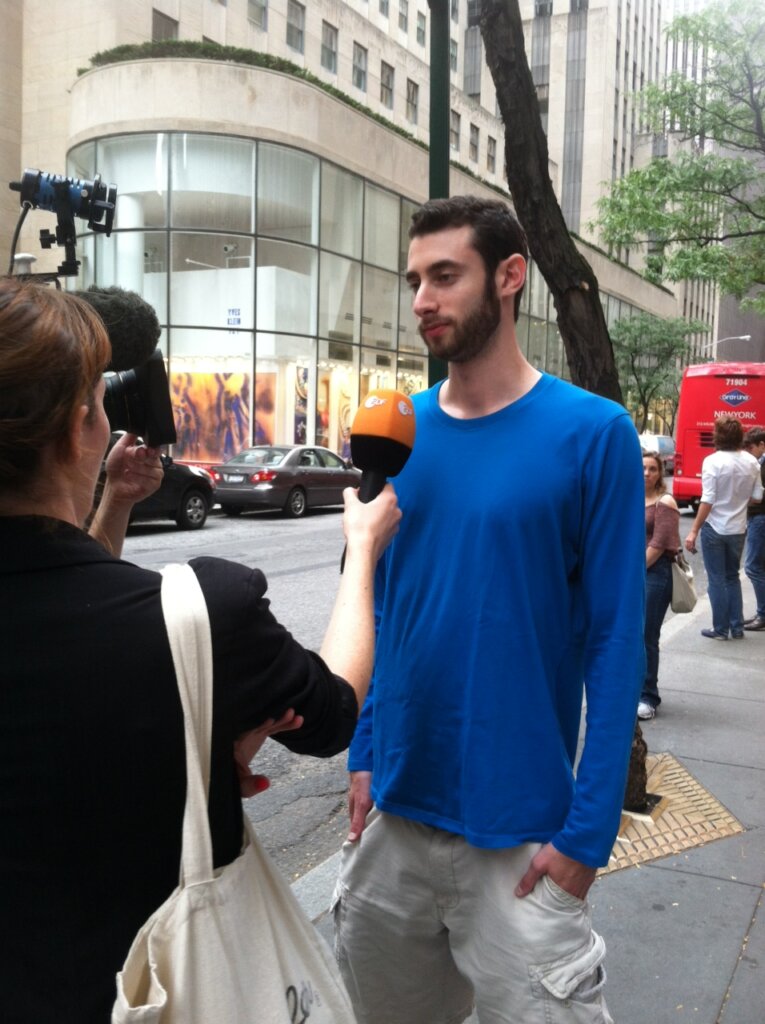 Edward Sturm in a blue shirt being interviewed by ZDF (Zweites Deutsches Fernsehen) in NYC near Rockefeller Center in 2012.